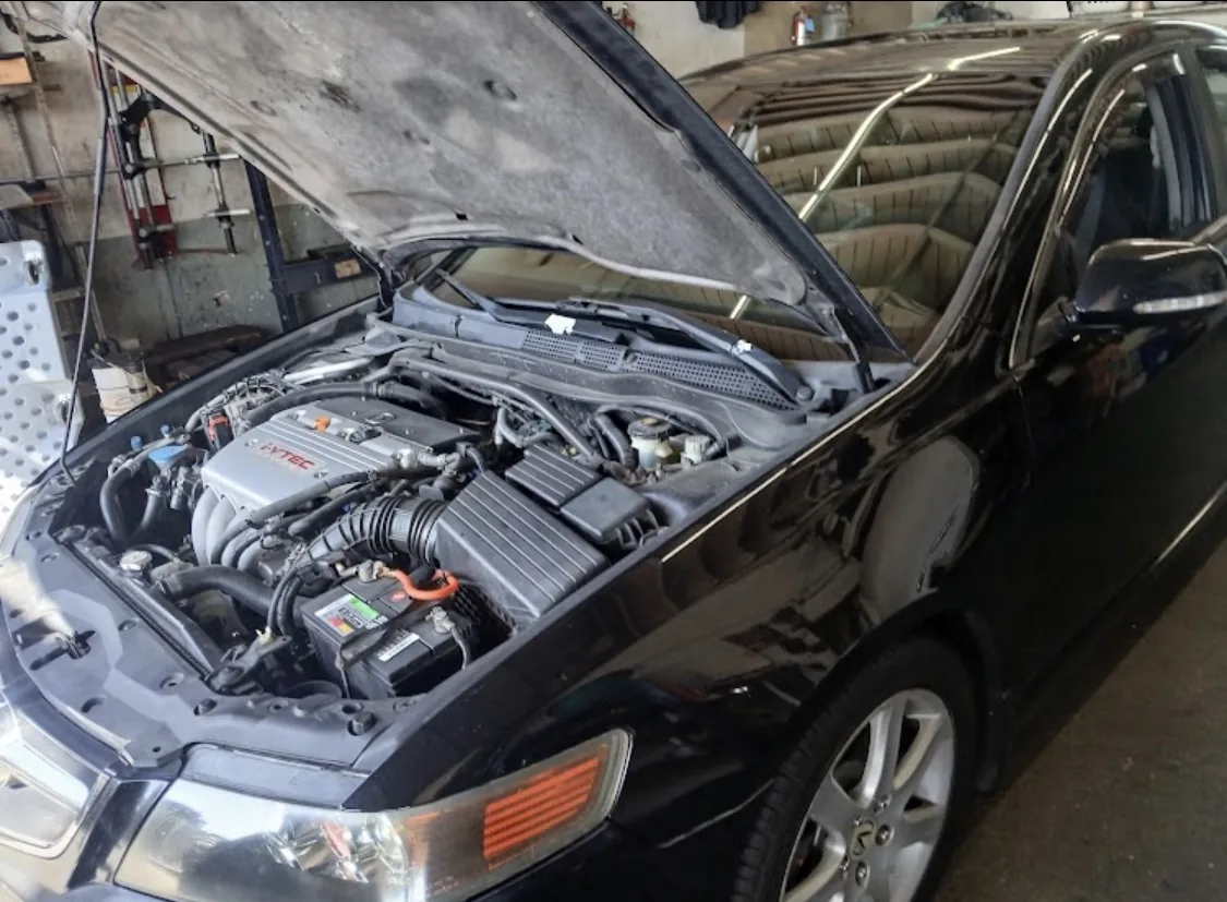 A black sedan raised in an EPI service bay with the hood up and engine exposed during service