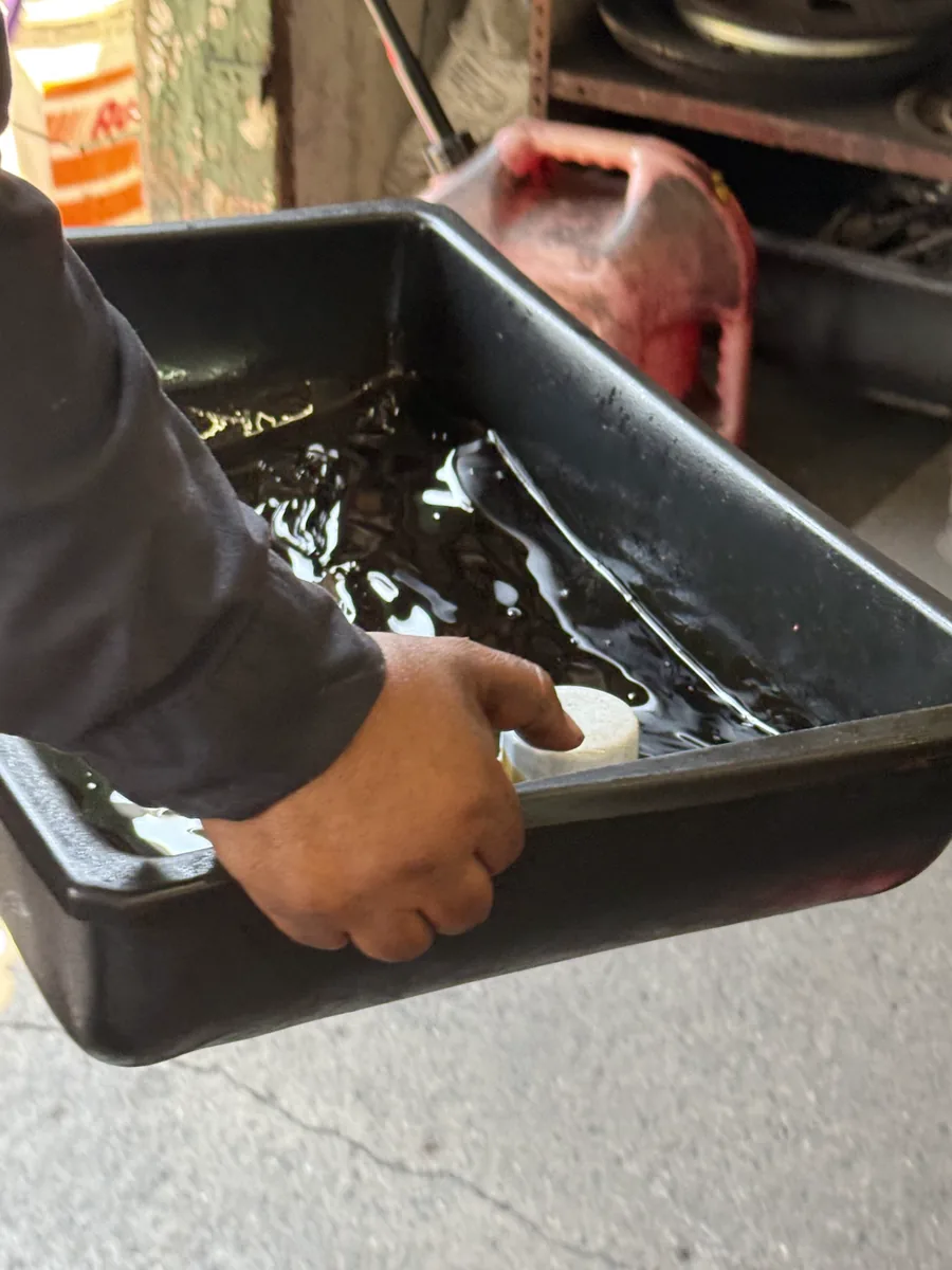 A technician's hand holding an oil drain pan with used motor oil and a fresh oil filter during an oil change at EPI Auto Service